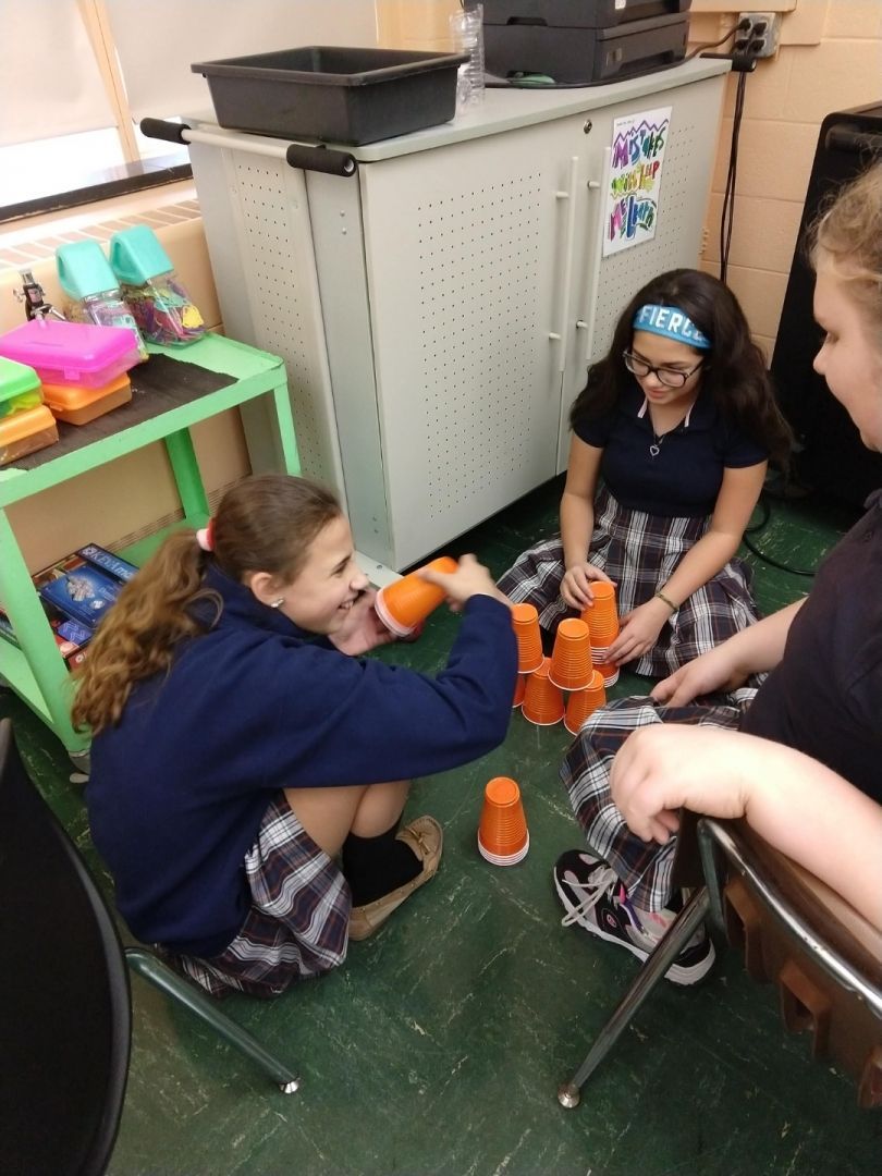 A group of young girls are sitting on the floor playing with cups