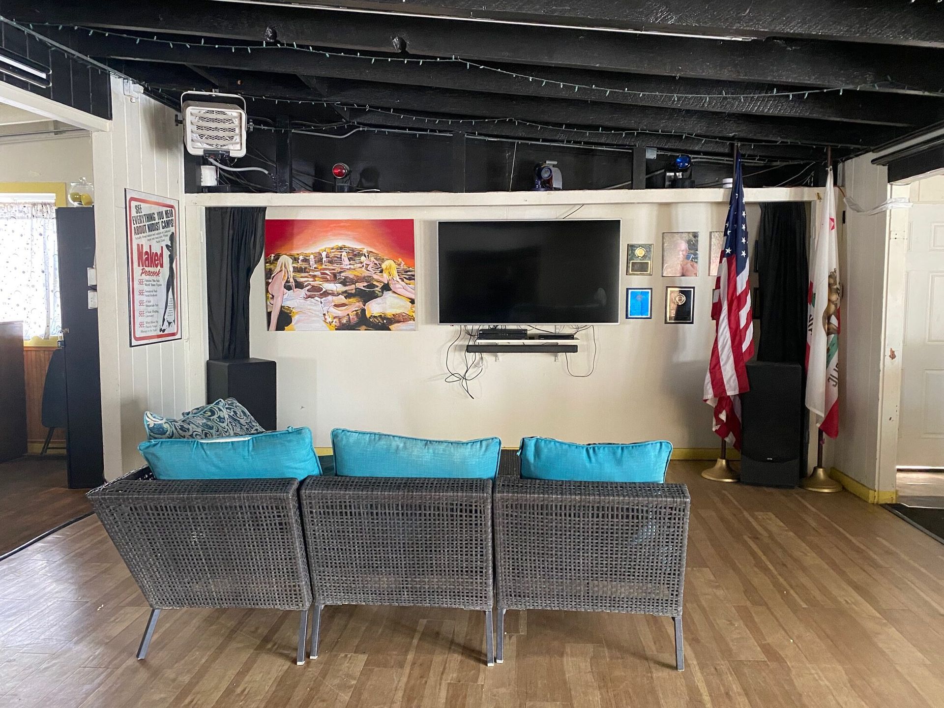 A living room with a couch facing a television mounted on a wall with posters and two flags.
