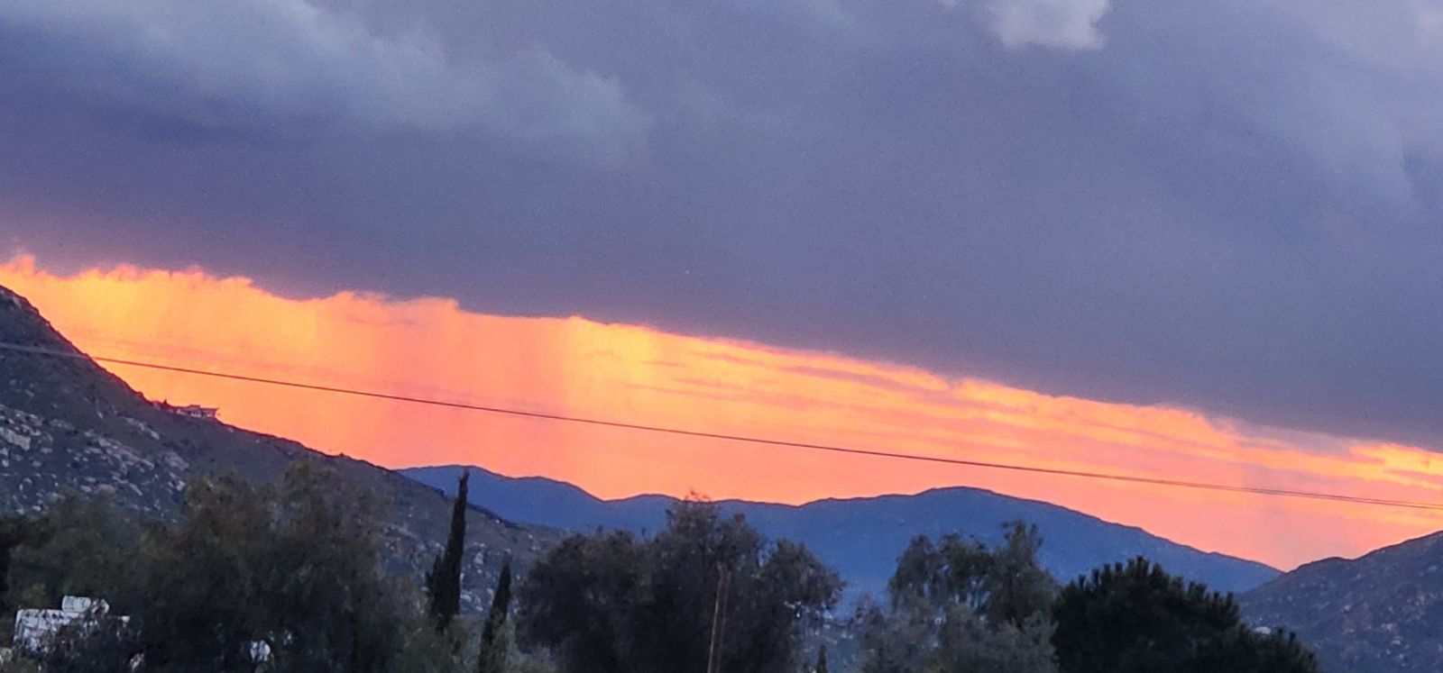 A vibrant sunset glows behind silhouetted mountains, with streaks of orange light casting a soft contrast against dark clouds.