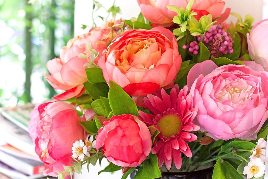 Bright bouquet of pink and coral flowers with green leaves in a basket near a sunlit window