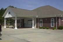 Brick building with white columns and covered entrance beside a large paved driveway