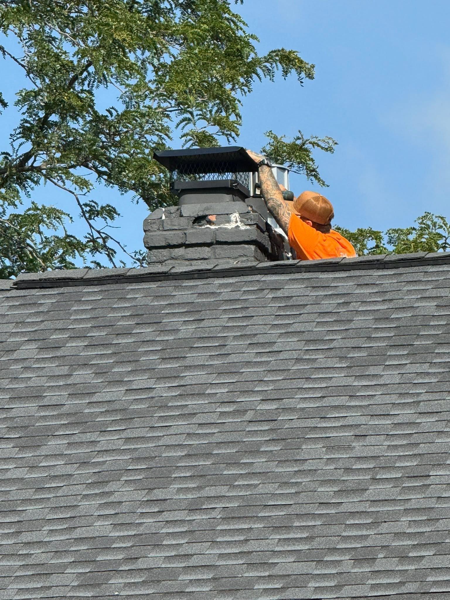 Gloved worker placing a black metal chimney cap on a brick rooftop vent