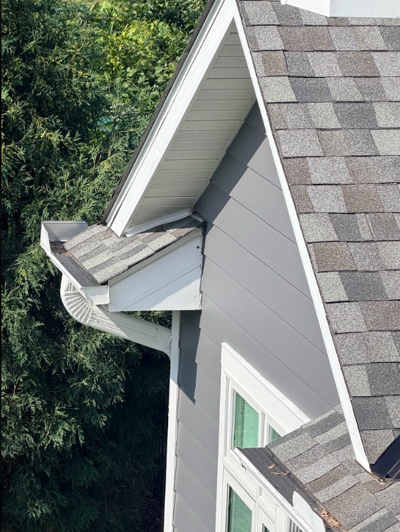 Gray house roof with dormer and shingles beside green trees