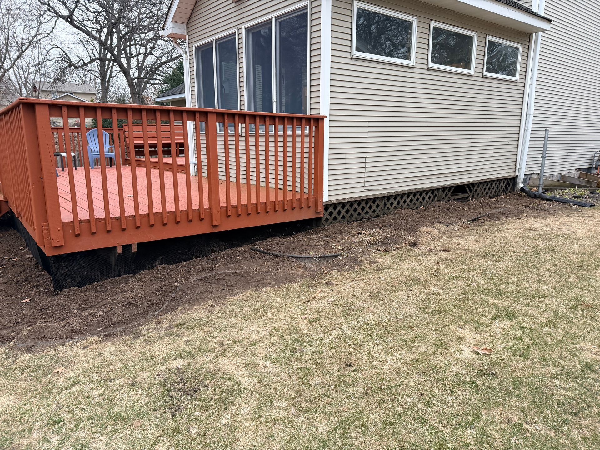 Wooden deck with red railing attached to a beige house beside a grassy yard