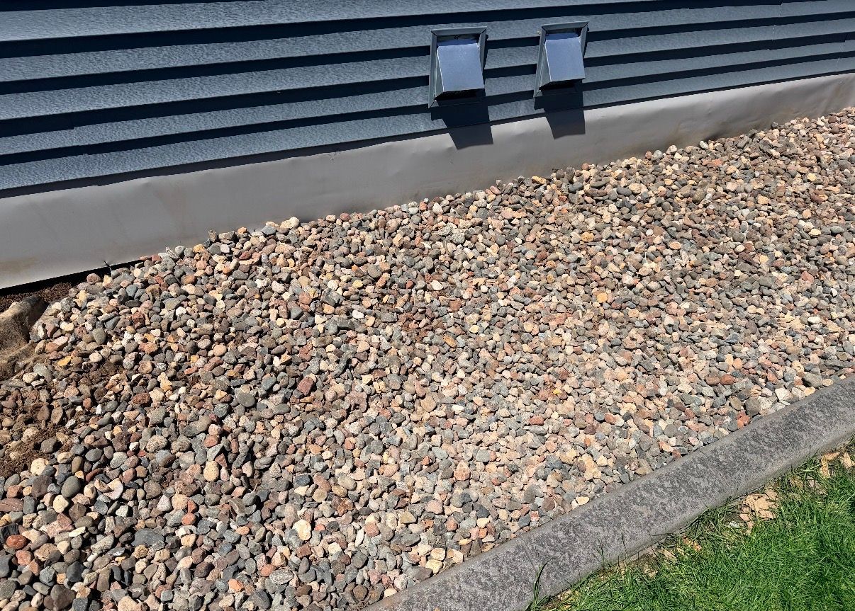 Rock-covered landscaping beside a dark blue house wall with two small exterior vents.