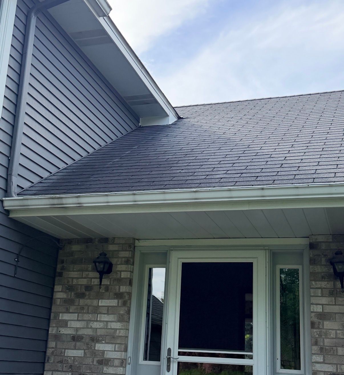 Front entrance of a house with gray siding, brick walls, and a shingled roof.