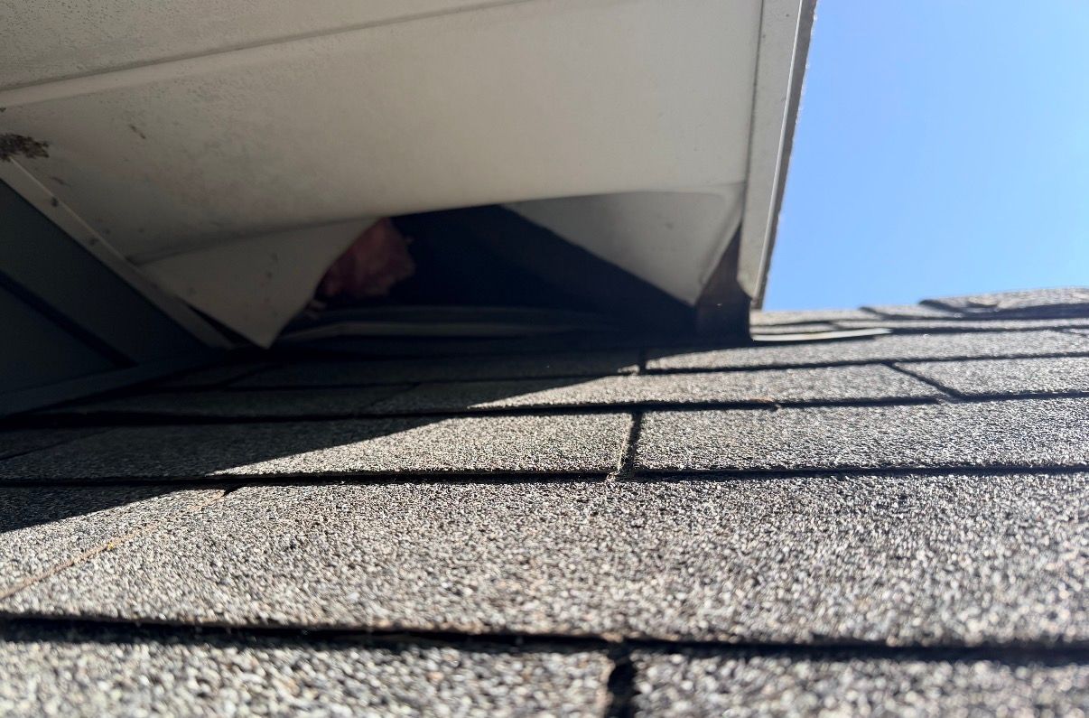 Close-up of a shingled roof with a roof vent against a blue sky