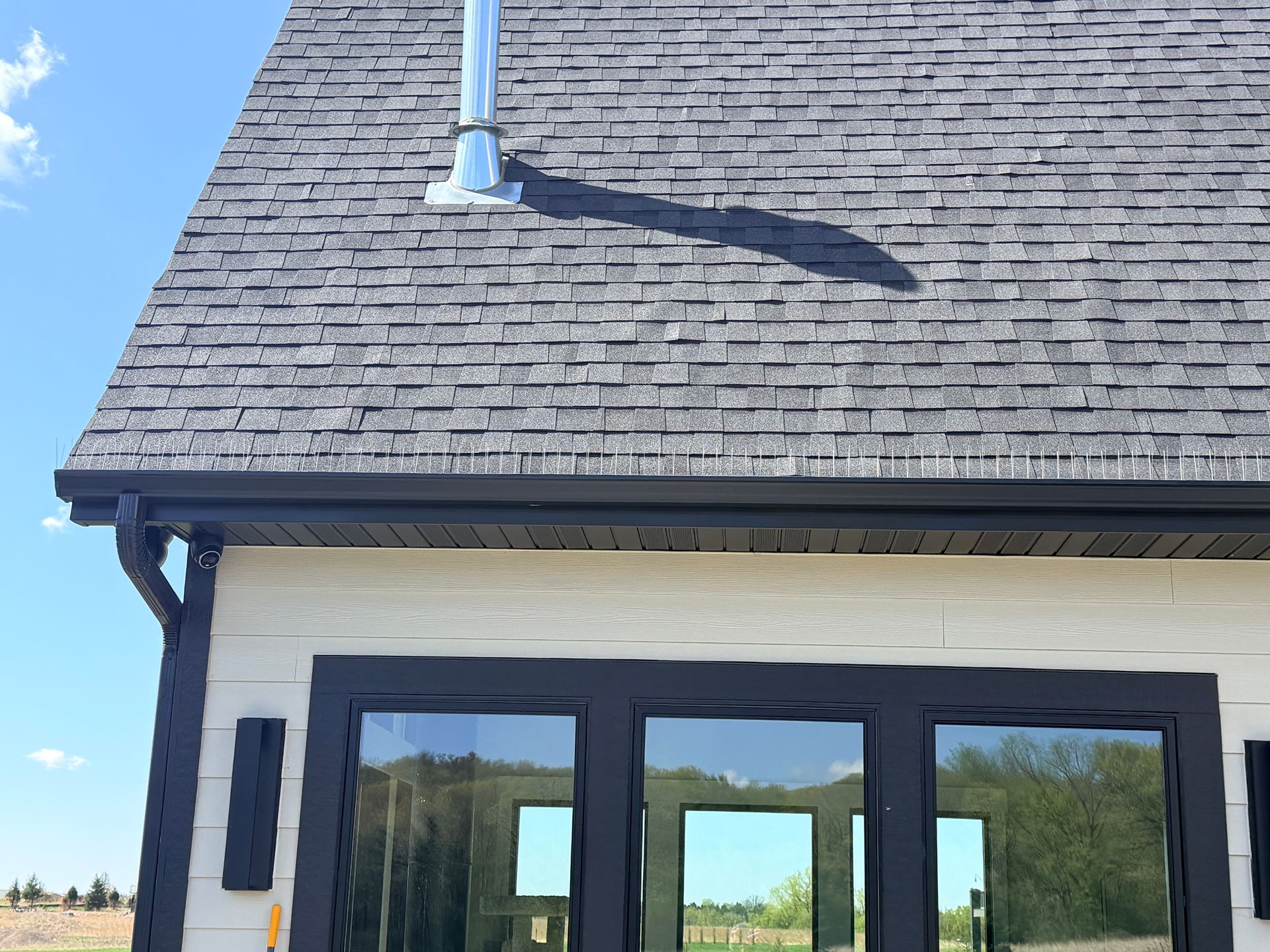 House exterior with gray shingle roof, black trim, and large windows under a blue sky
