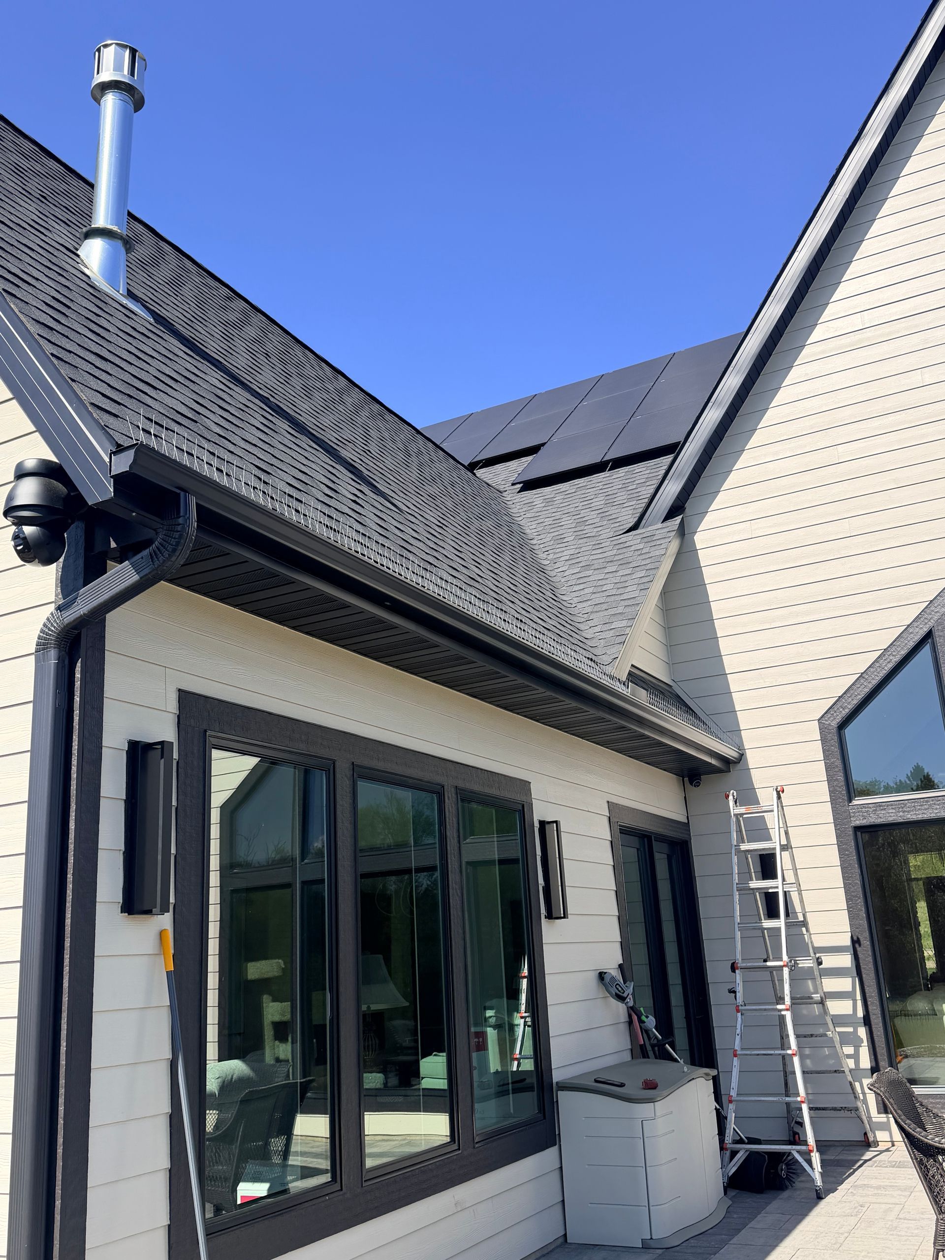 Modern house exterior with gray roof, black-framed windows, and beige brick walls beneath a blue sky
