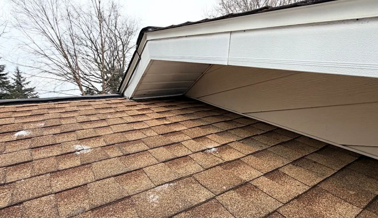 Roof shingles with roof edge and white overhang against a cloudy sky