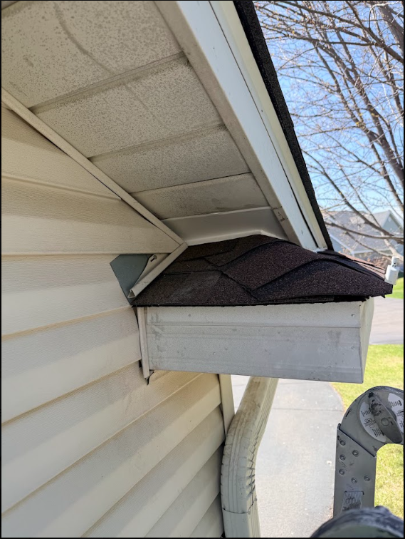 House eaves with a small shingled roof and vent box mounted beside beige siding