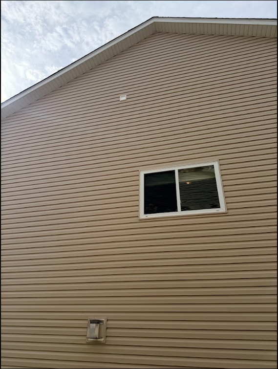 Beige house siding with a small window and roofline against a cloudy sky