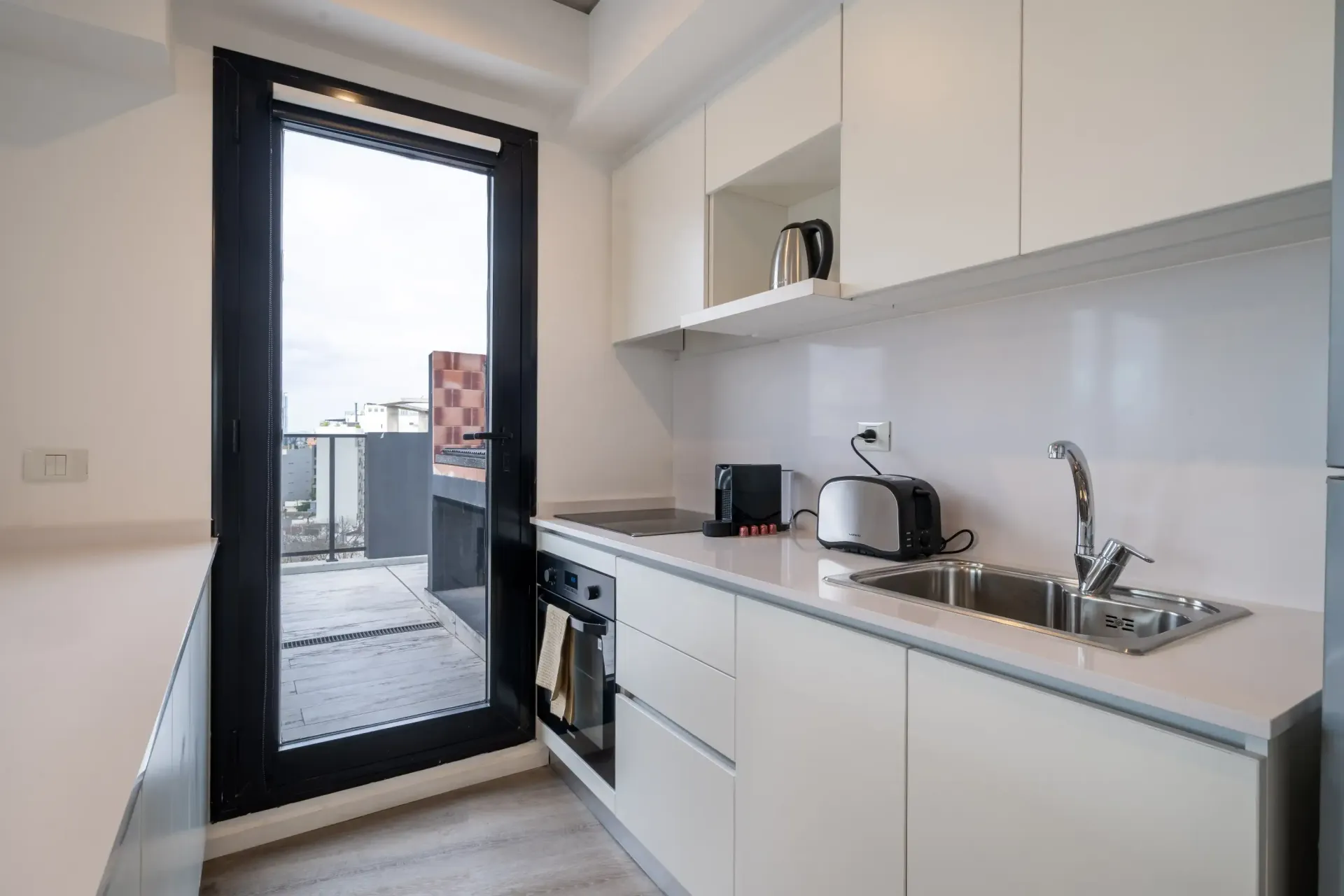 Una cocina con muebles blancos, un fregadero, un horno tostador y una ventana.