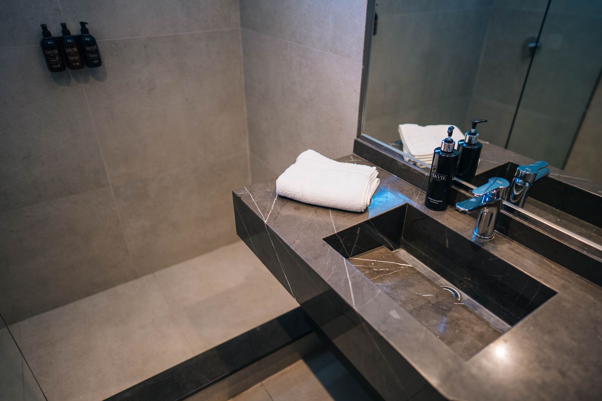 Baño moderno con lavabo de piedra gris, espejo, toalla y artículos de aseo.