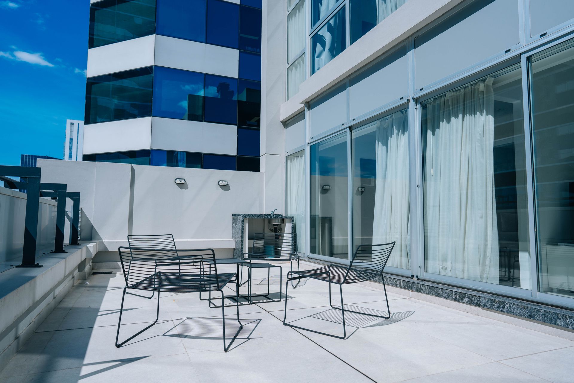 Patio exterior con muebles de metal frente a edificios altos en un día soleado.