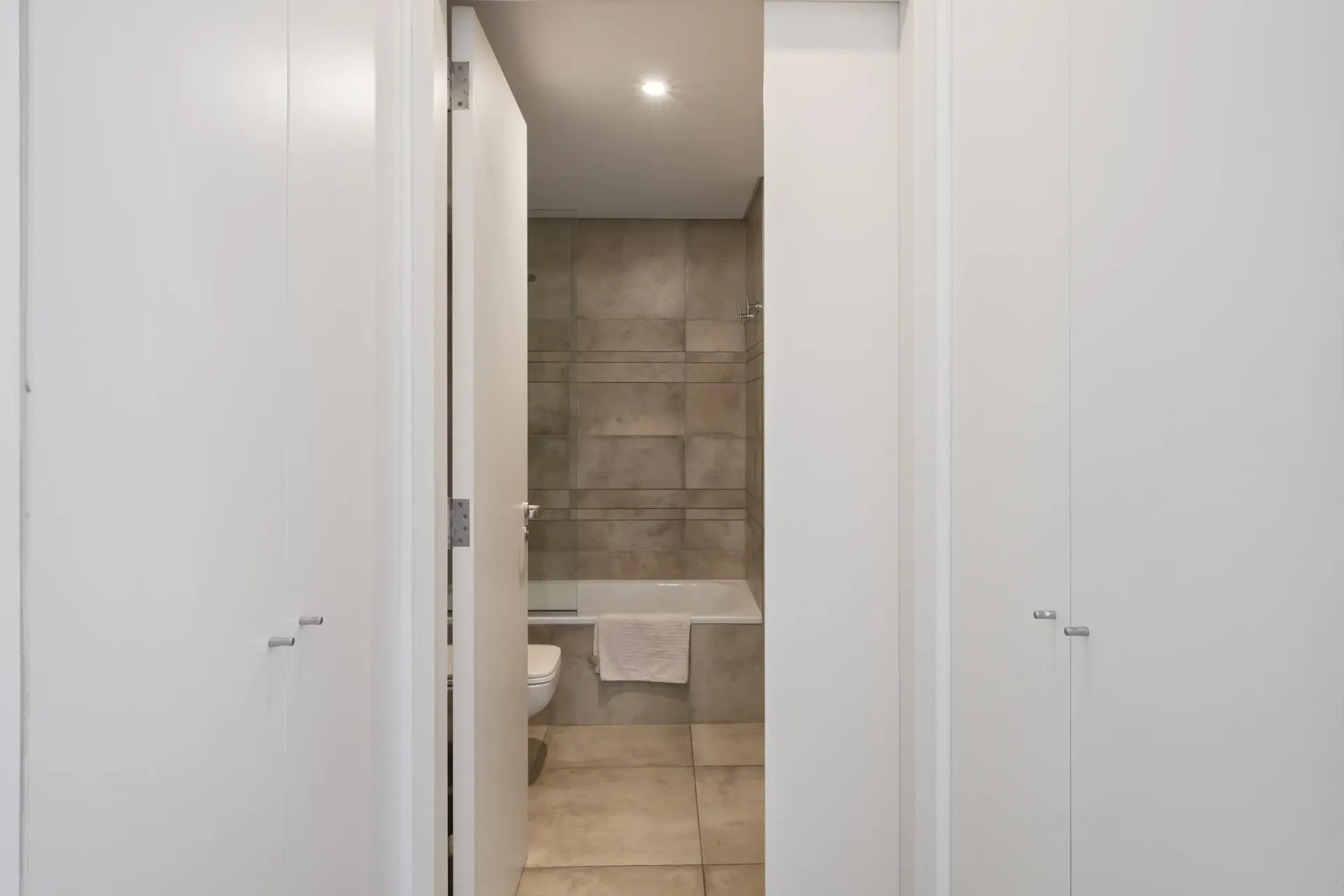 Un baño con bañera, inodoro y armarios blancos.