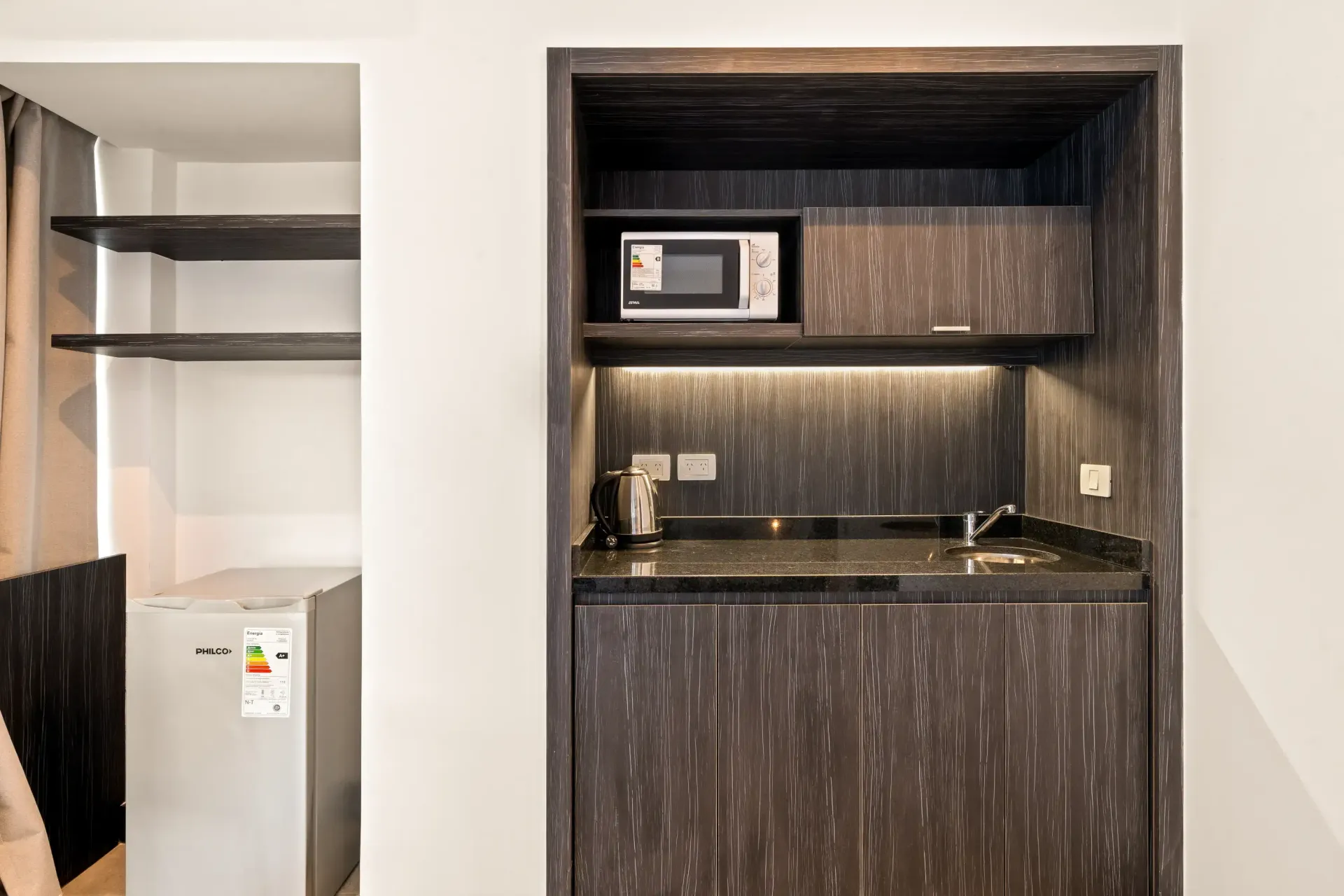 Una pequeña cocina con microondas y fregadero en una habitación de hotel.