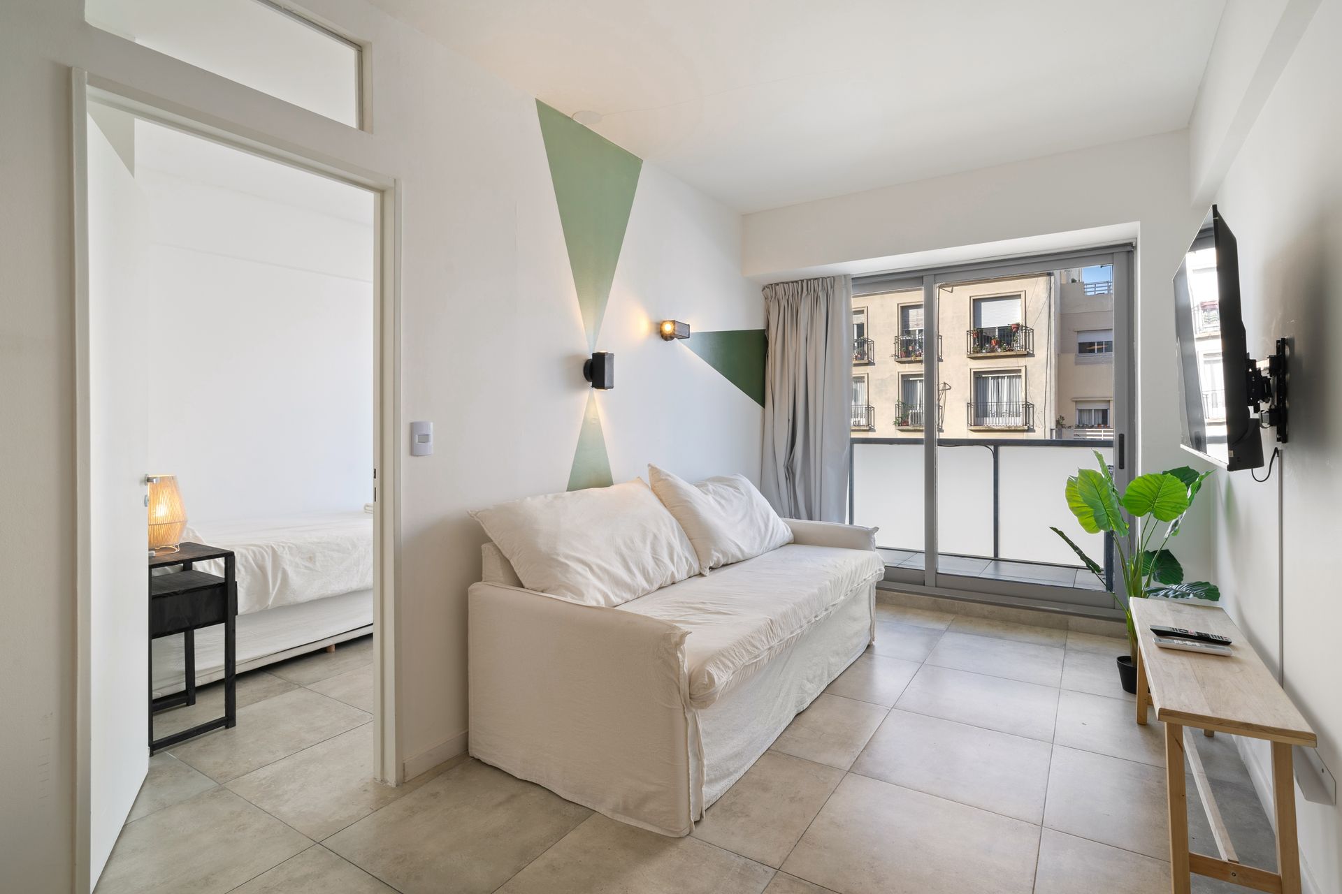 Un salón minimalista con un sofá blanco, una pequeña mesa consola de madera y vistas a un balcón.