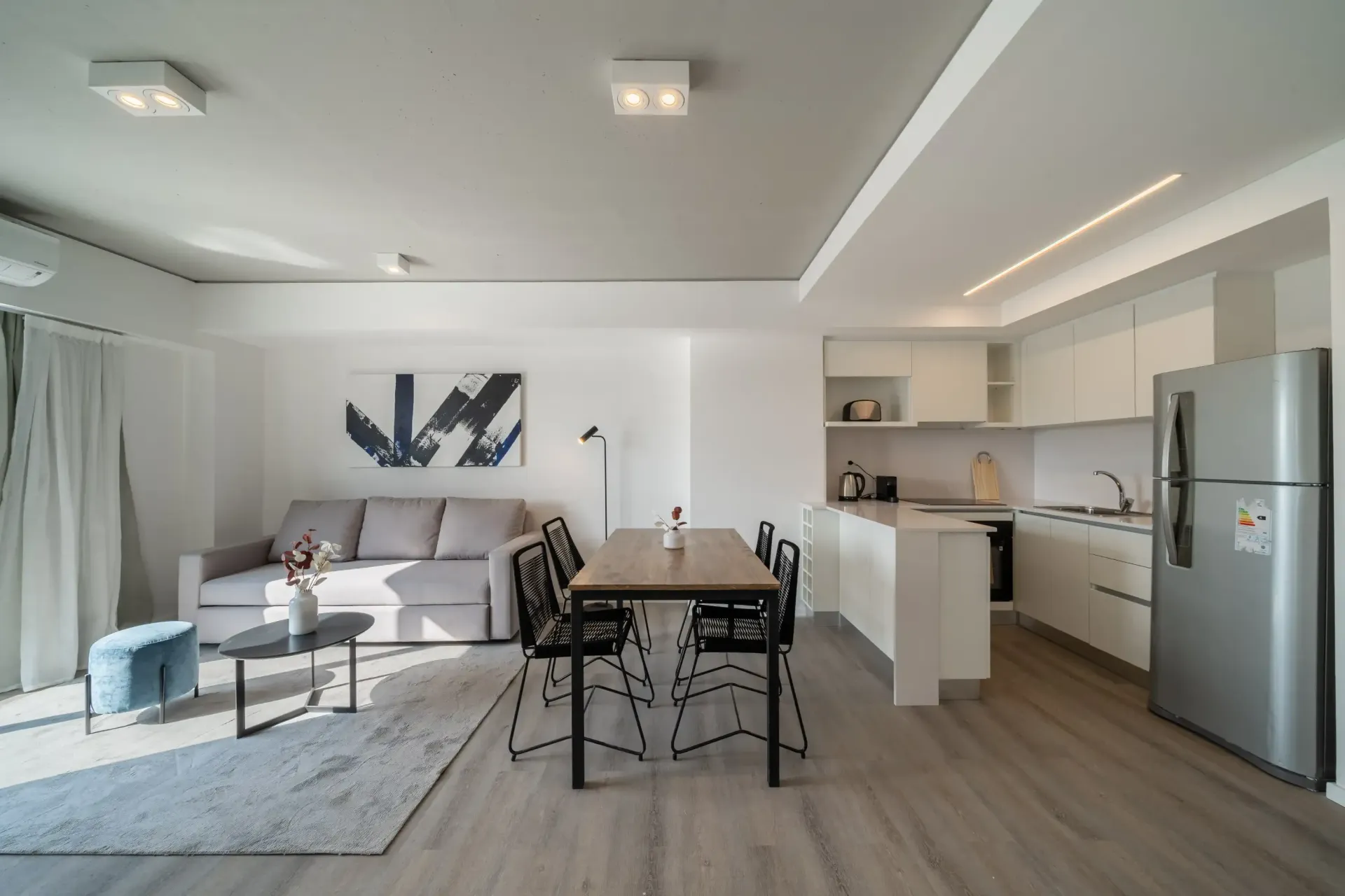 Una sala de estar con un sofá, una mesa, sillas y un refrigerador.