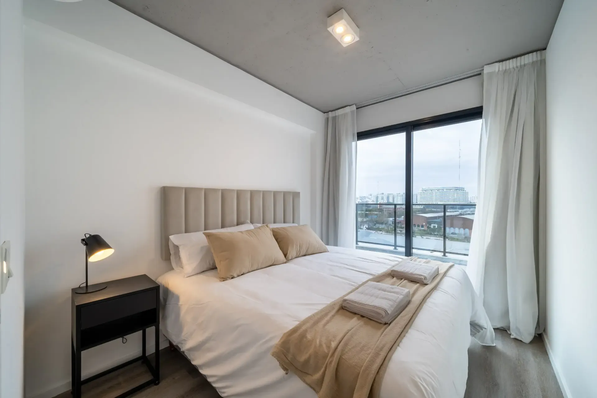 Un dormitorio con cama, mesita de noche, lámpara y puertas corredizas de vidrio.