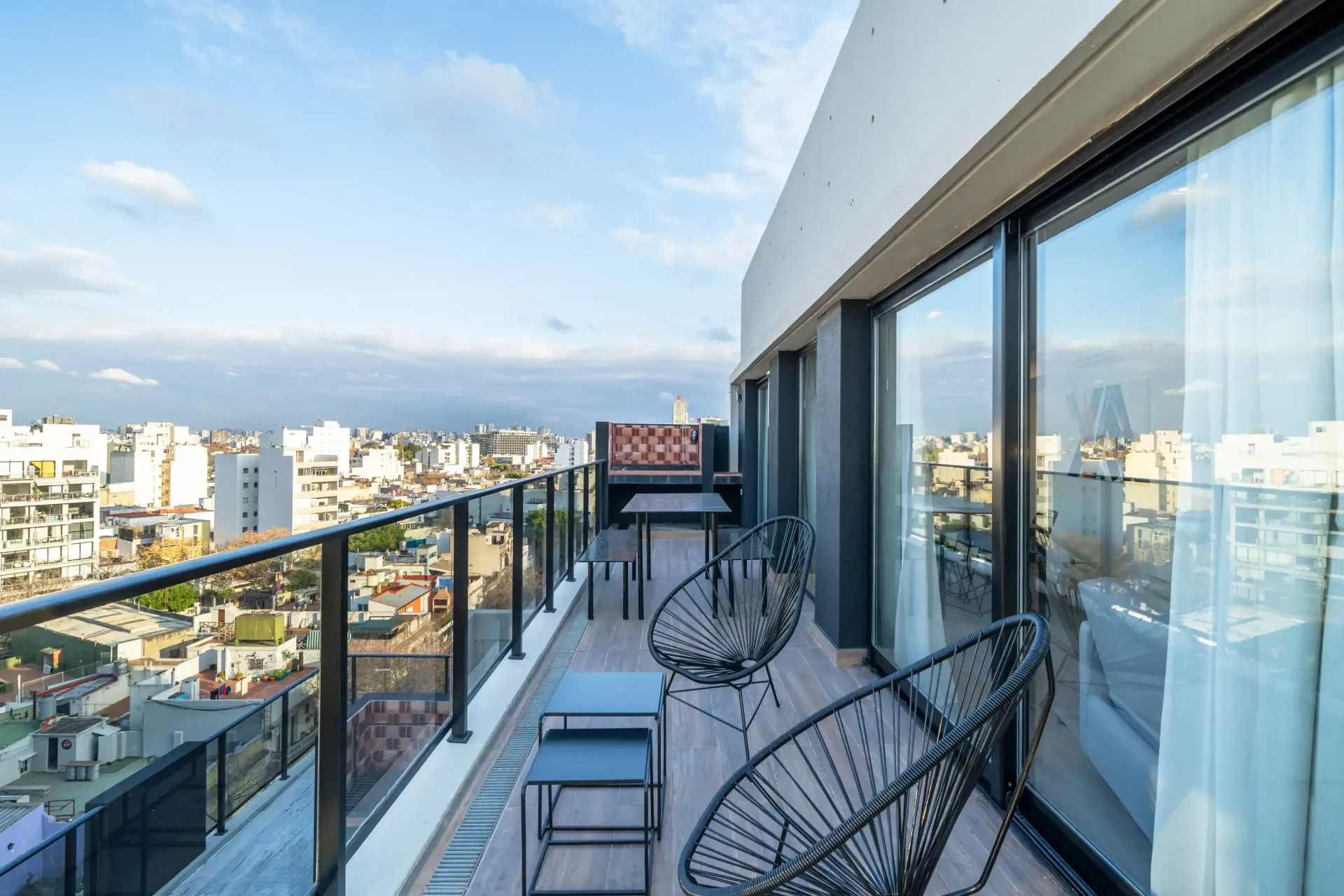 Un balcón con sillas y mesas con vista a una ciudad.