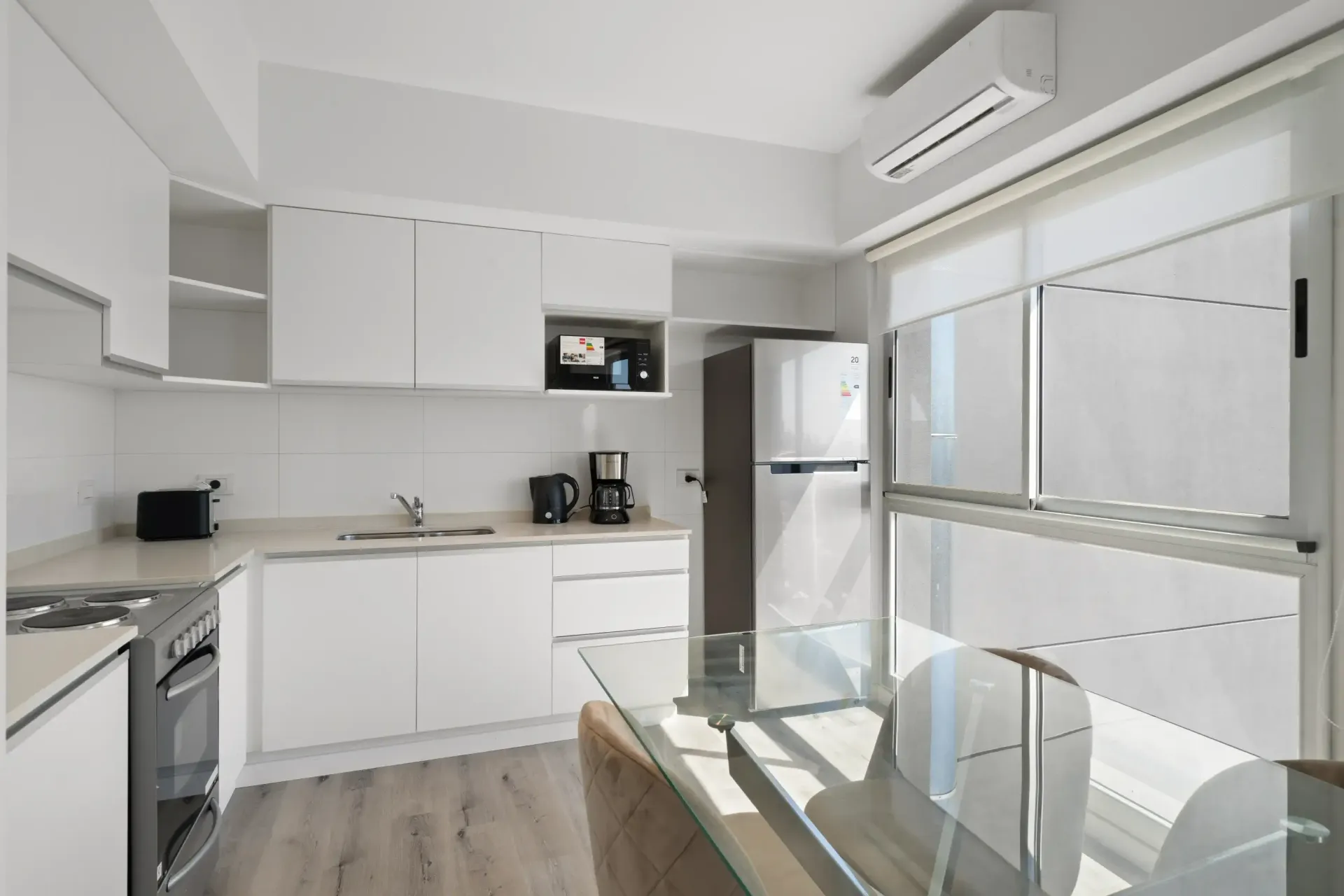 Una cocina con gabinetes blancos, electrodomésticos de acero inoxidable, un refrigerador y una mesa.