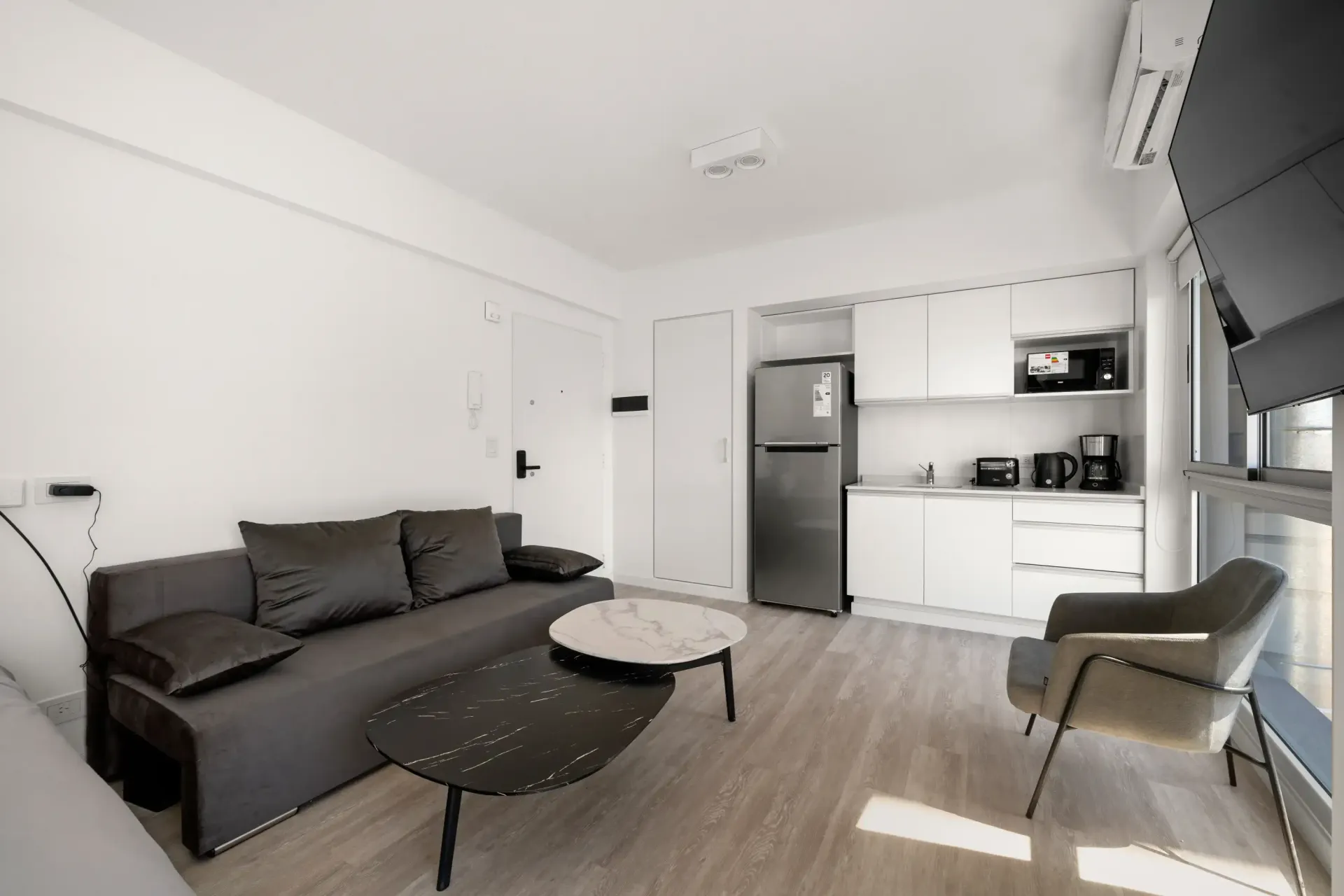 Una sala de estar con sofá, mesa, silla y refrigerador.