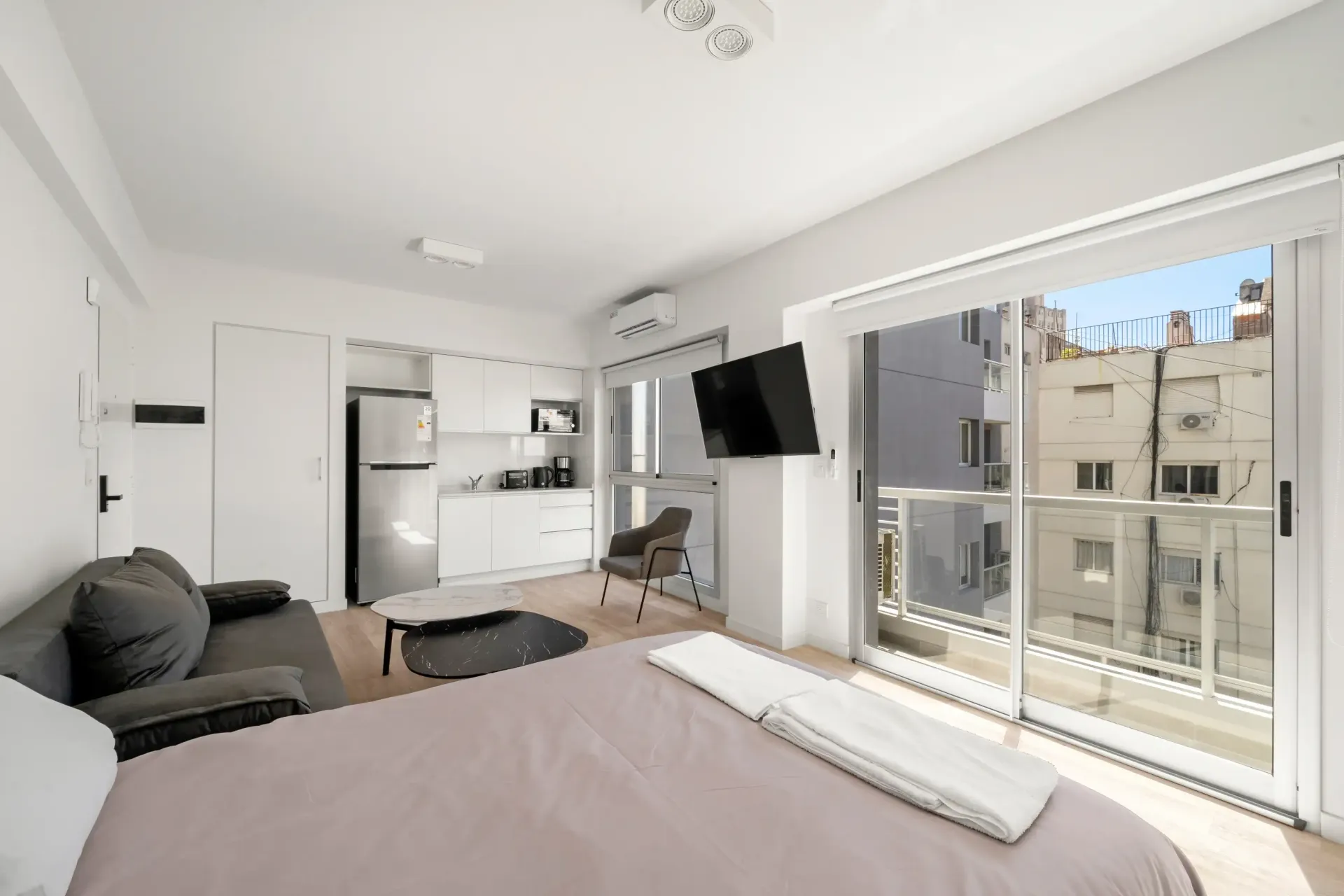 Un dormitorio con cama, sofá, televisión y balcón.