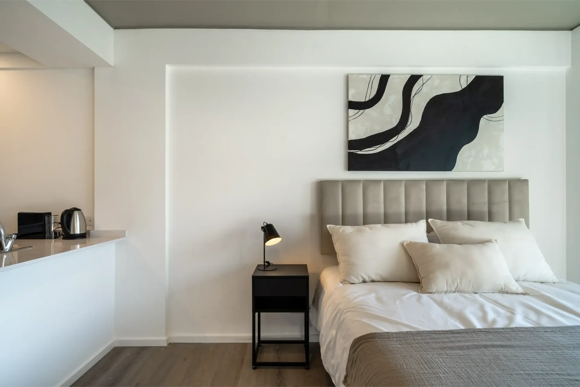 Un dormitorio con cama, mesita de noche, lámpara y cuadro en la pared.