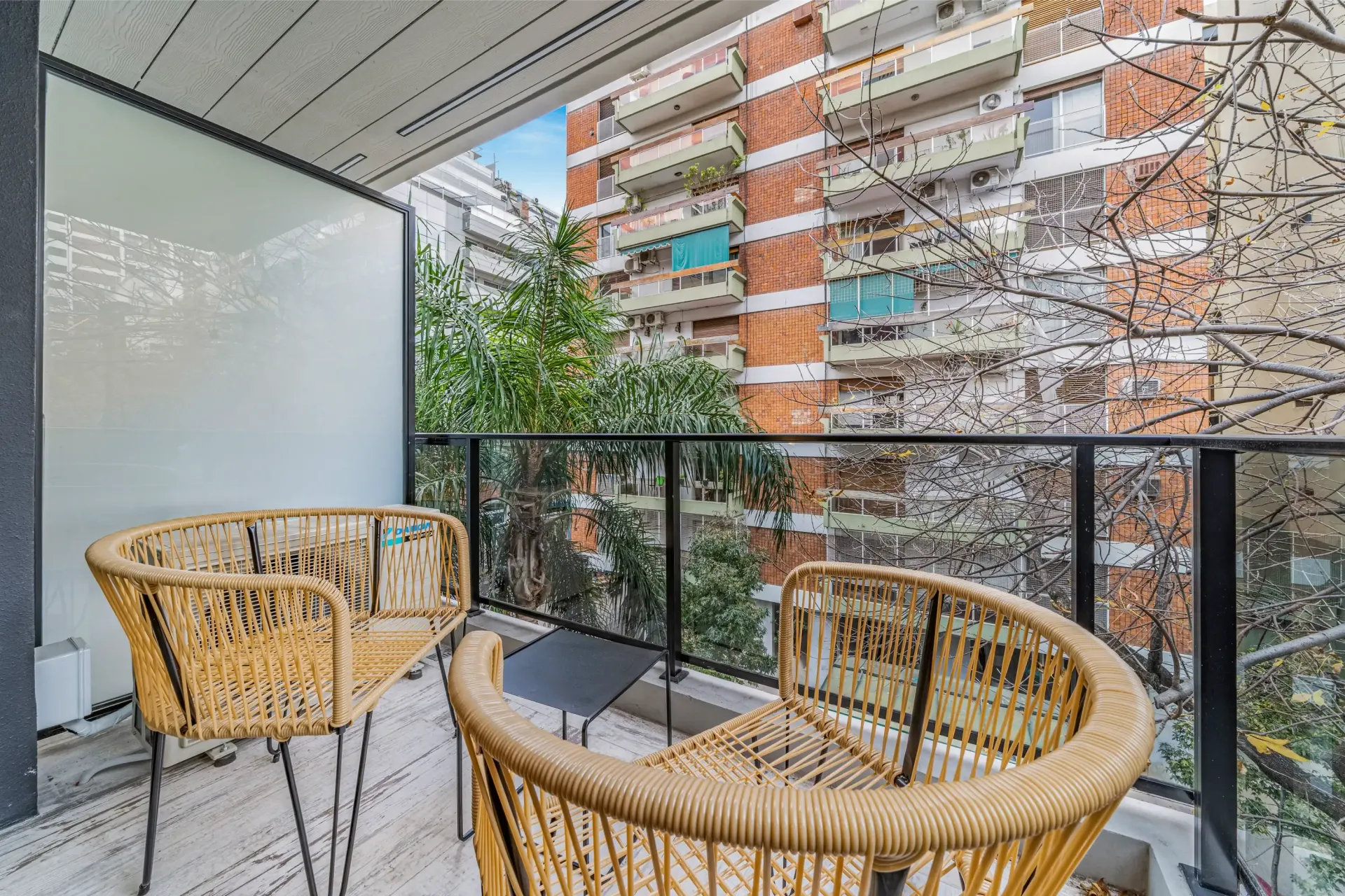Un balcón con dos sillas de mimbre y una mesa con vista a una ciudad.