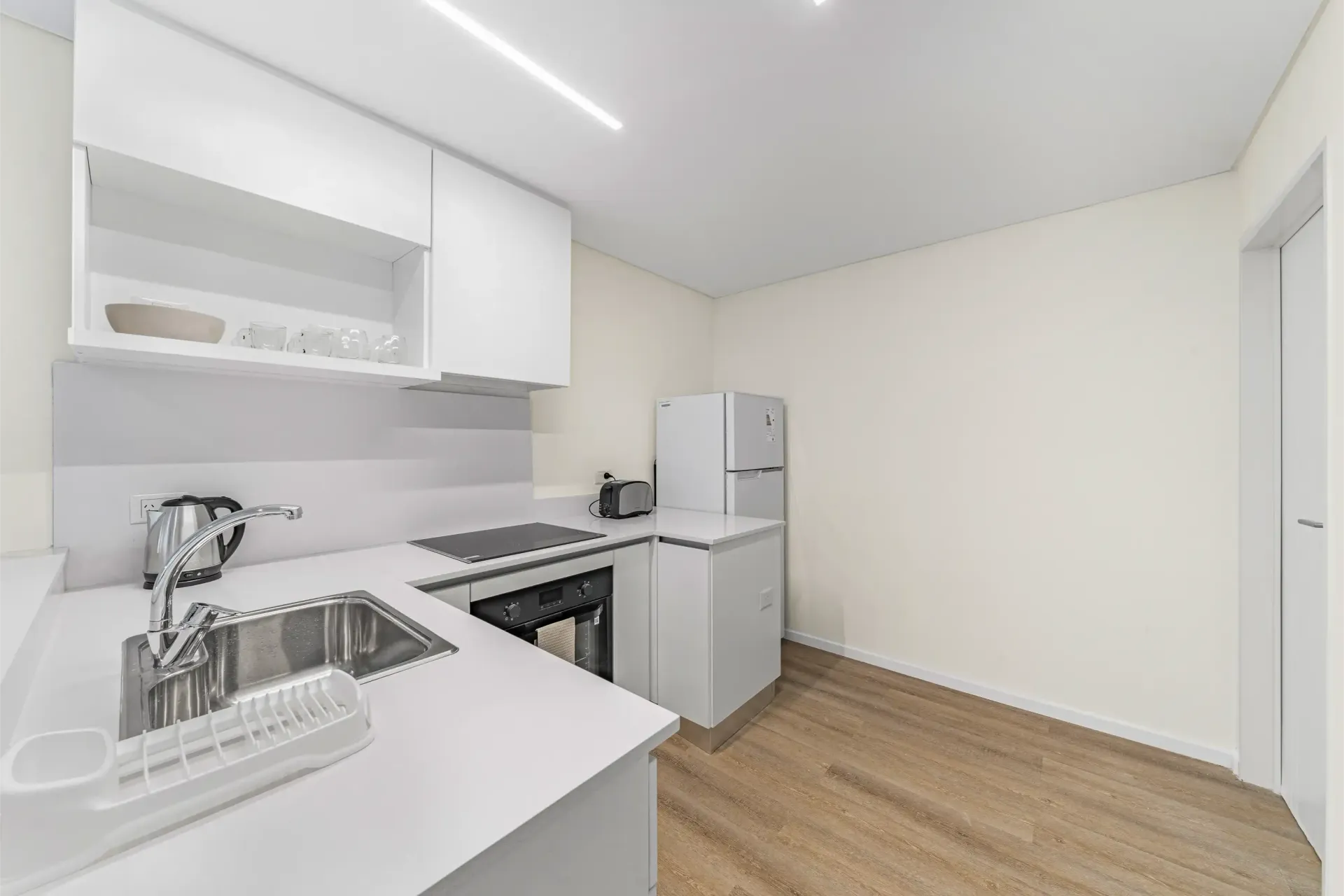 Una cocina con gabinetes blancos, un fregadero y un refrigerador.