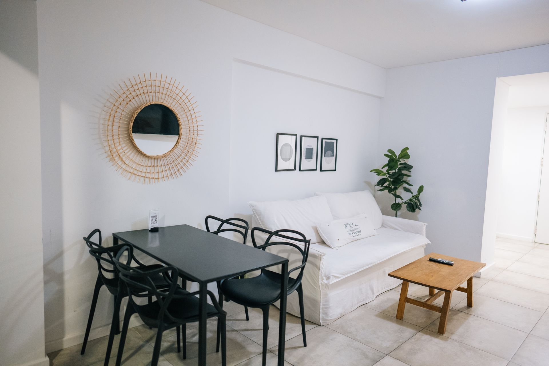 Un moderno salón-comedor con un sofá blanco, una mesa de comedor negra con cuatro sillas negras y un espejo decorativo.
