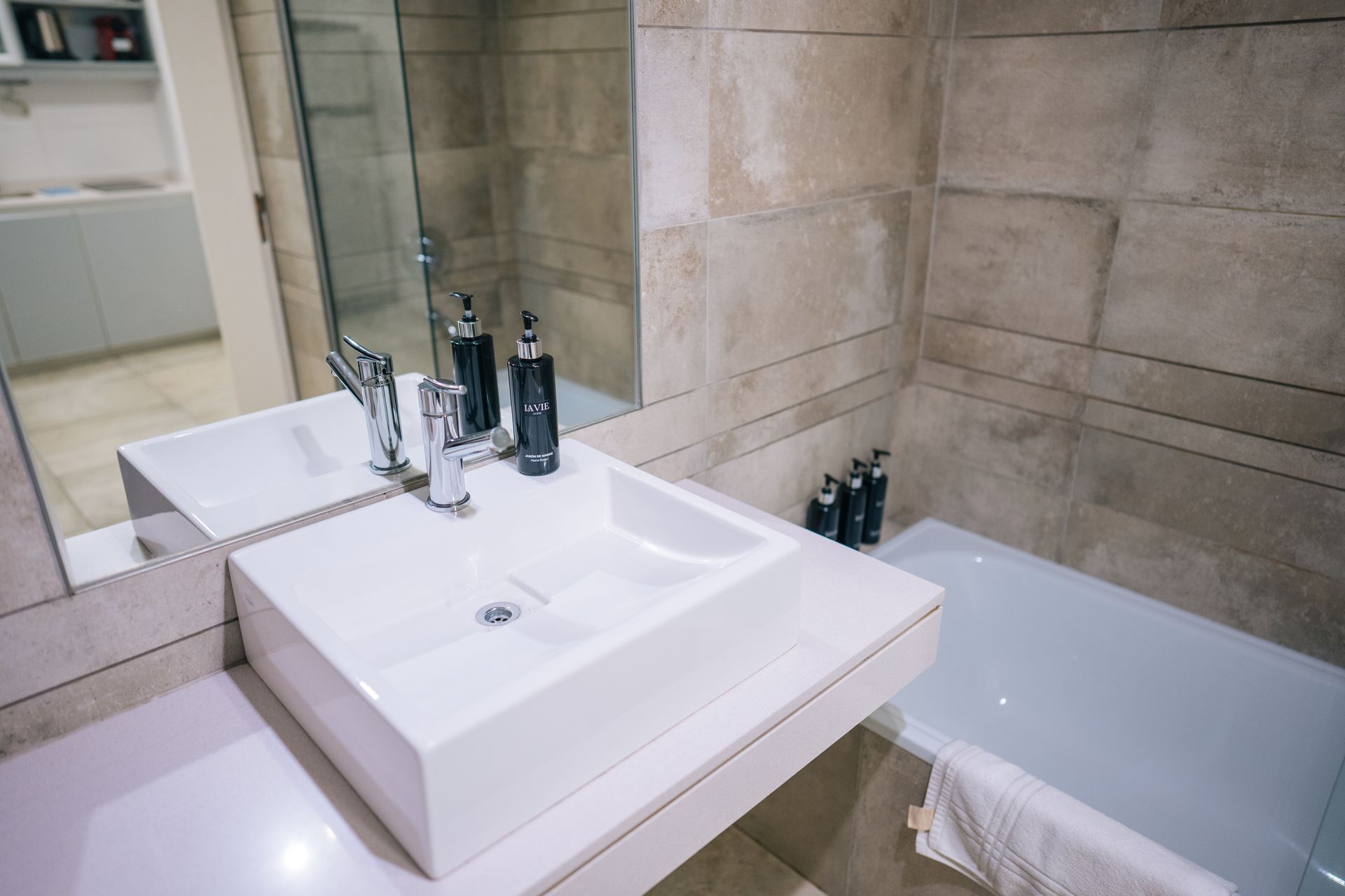 Un baño moderno con lavabo rectangular blanco, grifo cromado y pared alicatada sobre la bañera.
