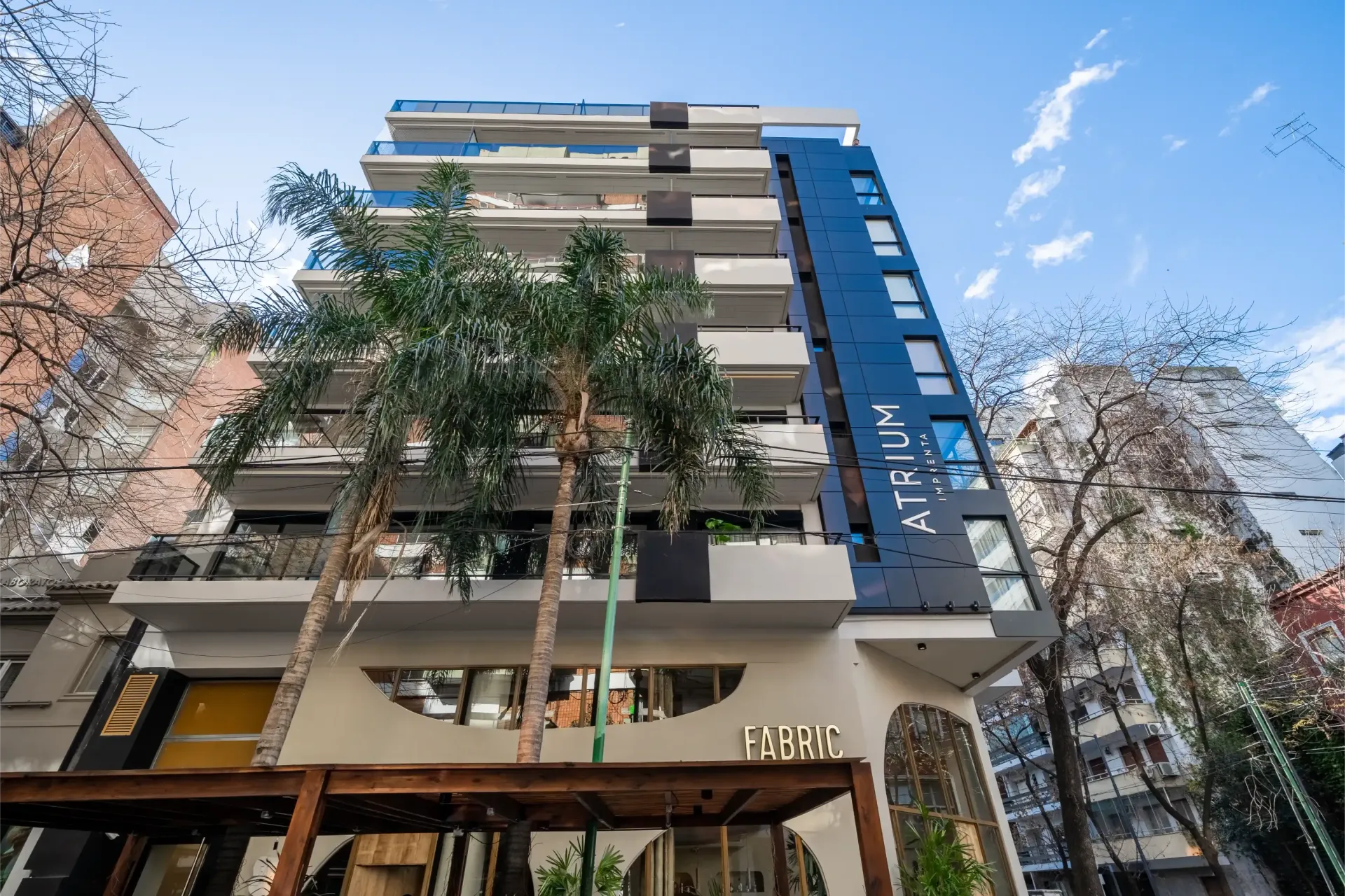 Un edificio alto con muchas ventanas y balcones está rodeado de árboles.