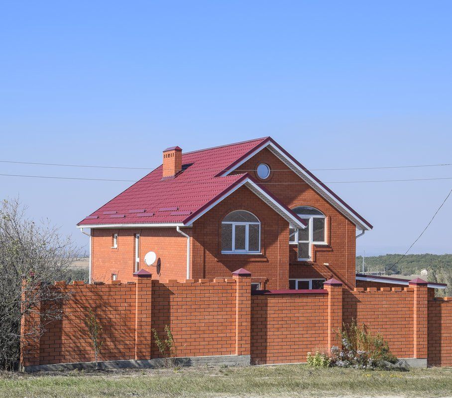 Red brick house with a red roof behind a brick fence on a clear day