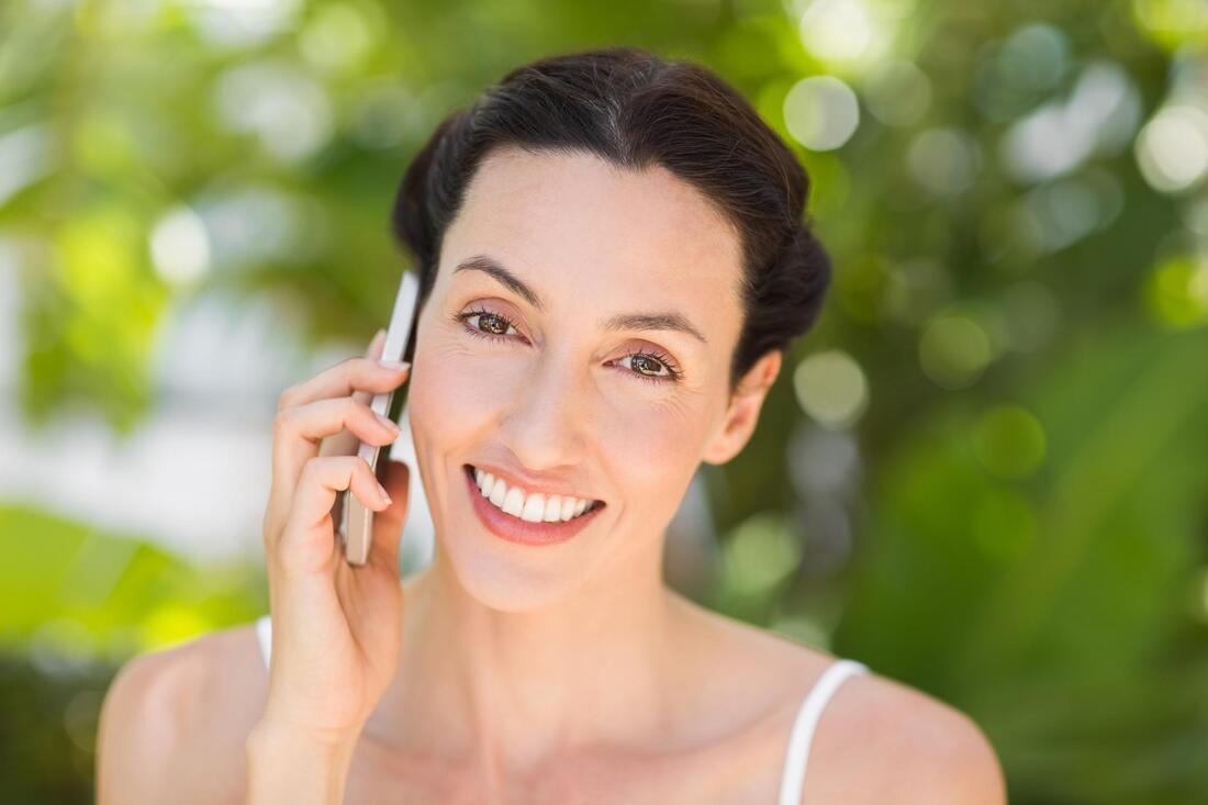 Smiling person holding a phone outdoors against a blurred green background