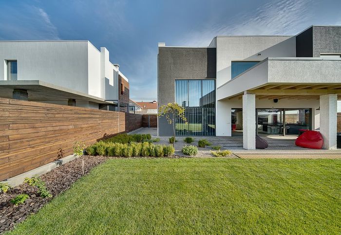 Modern house exterior with green lawn, wood fence, and covered patio under a blue sky