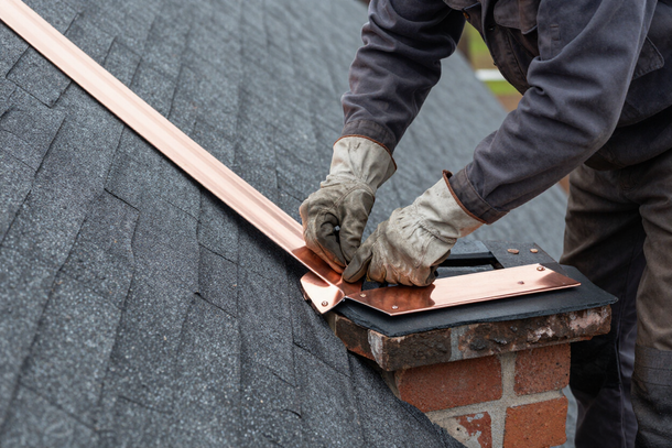 Copper step flashing installation at chimney-roof junction