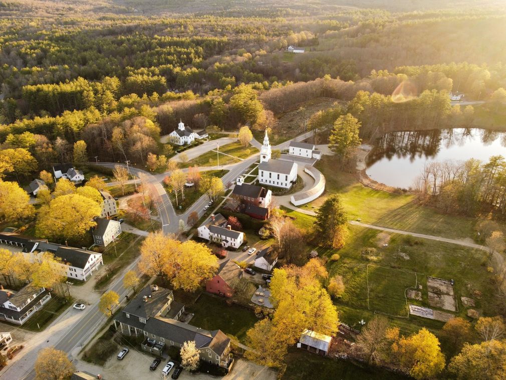 Aerial view of a small church village surrounded by autumn trees and a lake at sunset