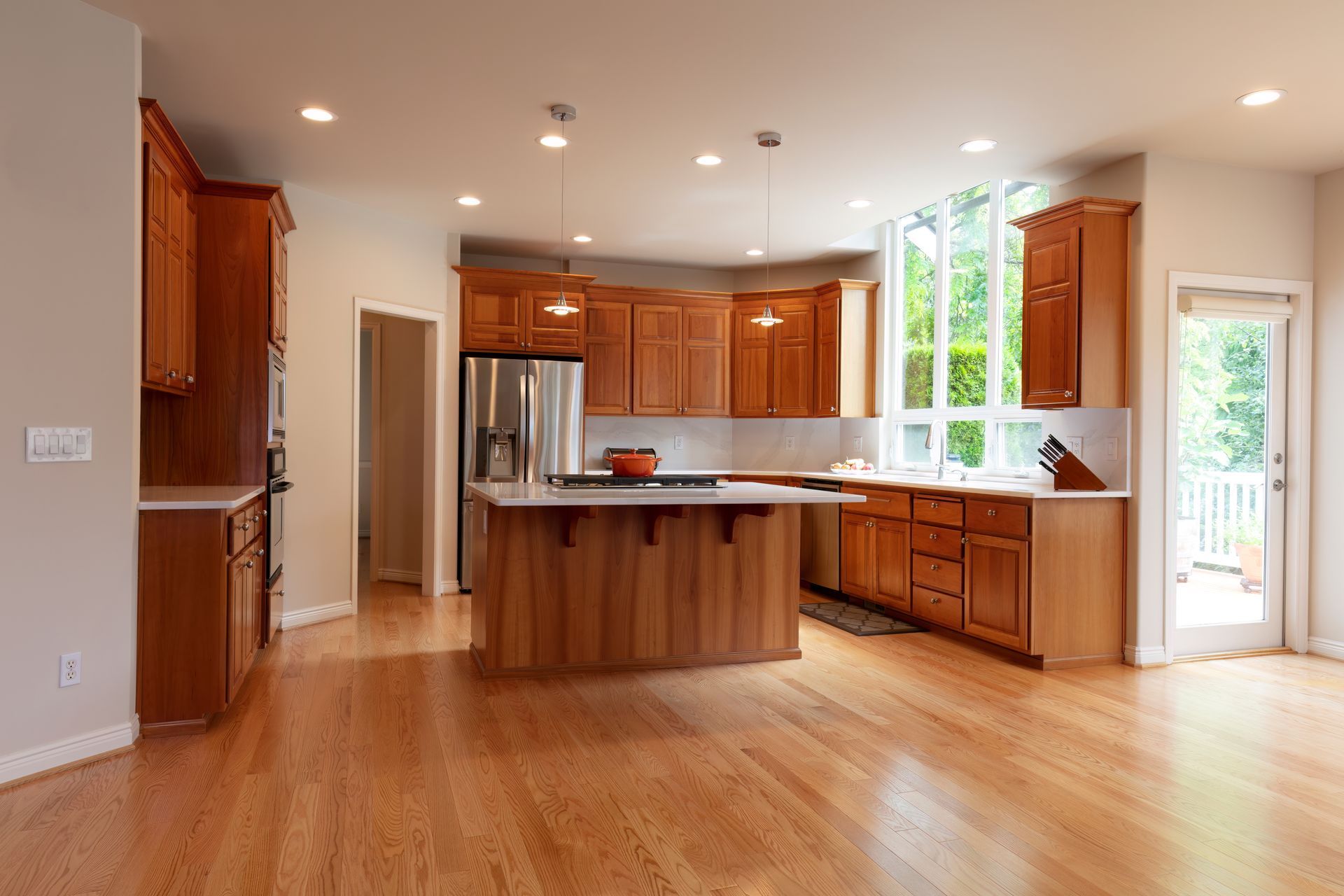 A bright kitchen with light-colored walls, natural wood cabinets, a large island, stainless appliances, and wood floors.