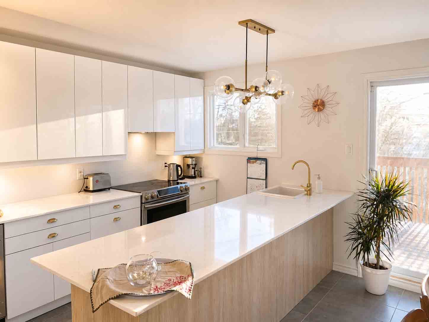 Cuisine blanche moderne avec un grand îlot et une suspension; une pièce ensoleillée avec une porte donnant sur l'extérieur.