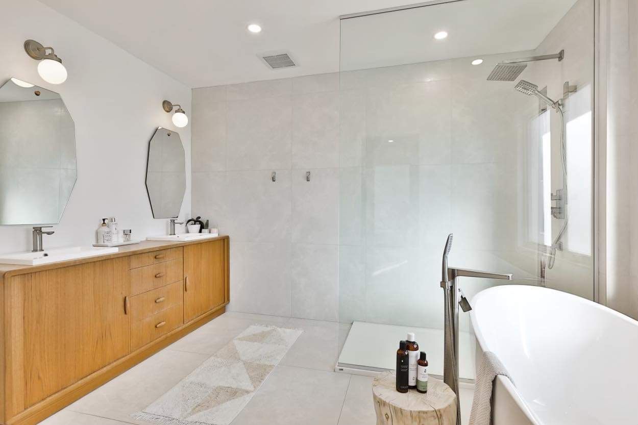 Salle de bain moderne et blanche lumineuse avec vanité en bois, douche à l'italienne et baignoire autoportante.