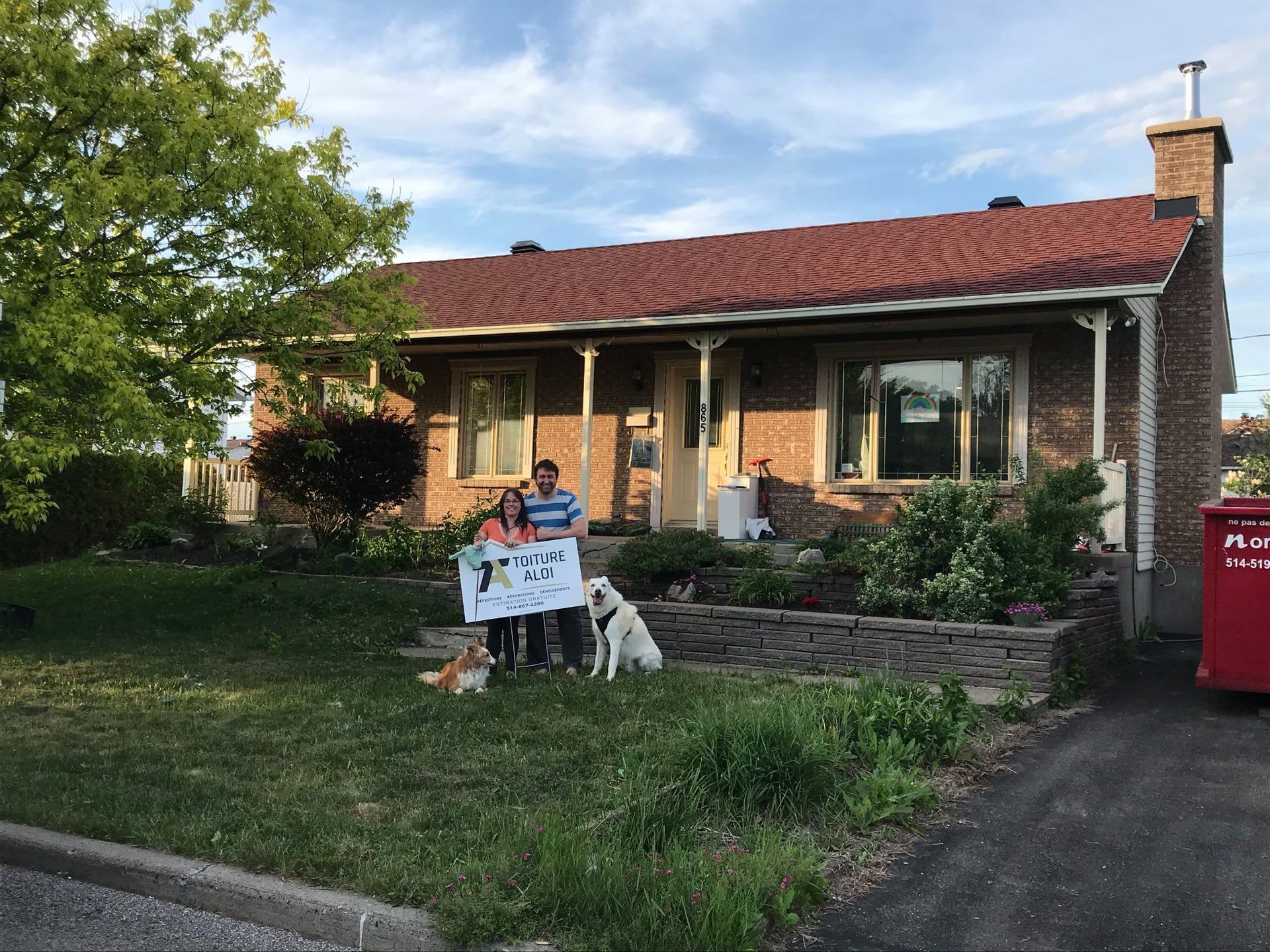 Un couple debout devant une maison tenant une pancarte.