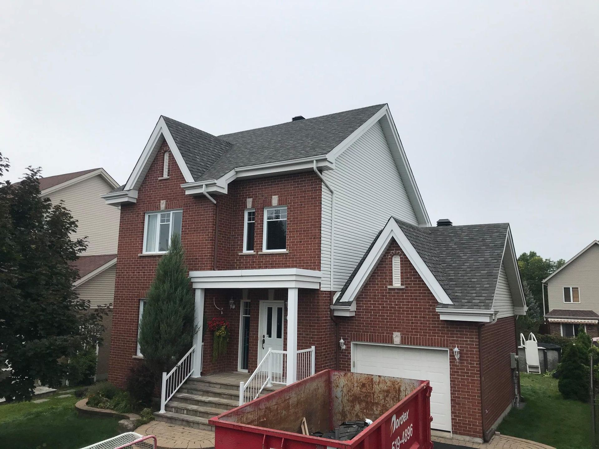 Une grande maison en briques avec une benne à ordures rouge devant.