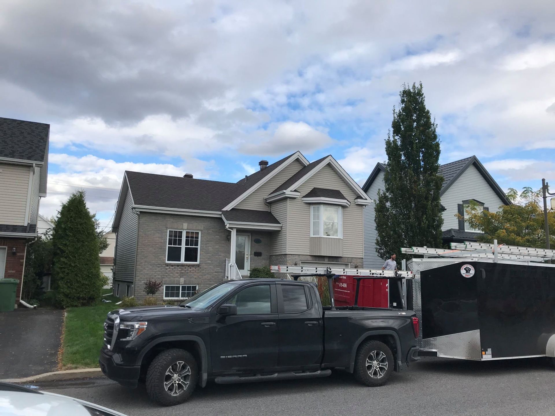 Un camion noir est garé devant une maison avec une remorque attachée.