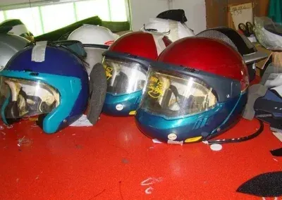 Su una superficie rossa sono appoggiati diversi caschi da motociclista, di colore blu e rosso, con uno sfondo interno sfocato.