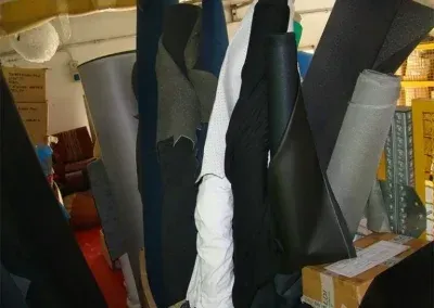Un'area di stoccaggio verticale piena di rotoli di tessuto e pelle di vario tipo, nelle tonalità del nero, del grigio, del bianco e del blu.