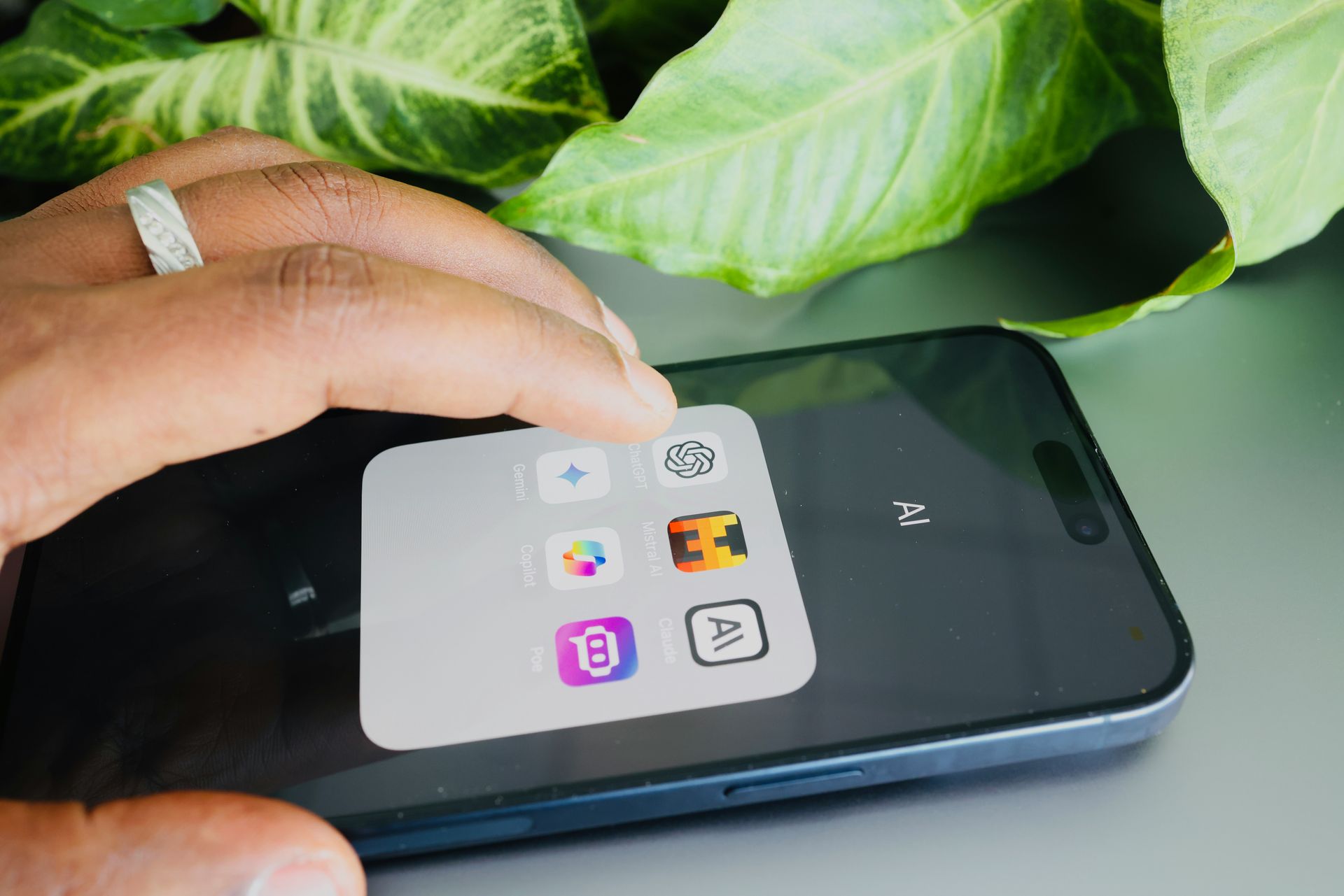 Person's hand tapping a collection of app icons on a smartphone screen, with a green plant in the background.