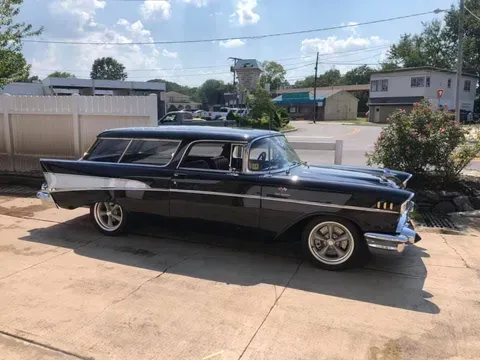 An old black station wagon is parked in a driveway.