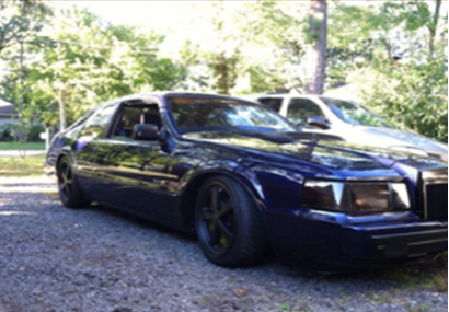 A blue car is parked in a gravel driveway